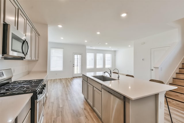 kitchen featuring a kitchen breakfast bar, appliances with stainless steel finishes, sink, gray cabinetry, and a center island with sink