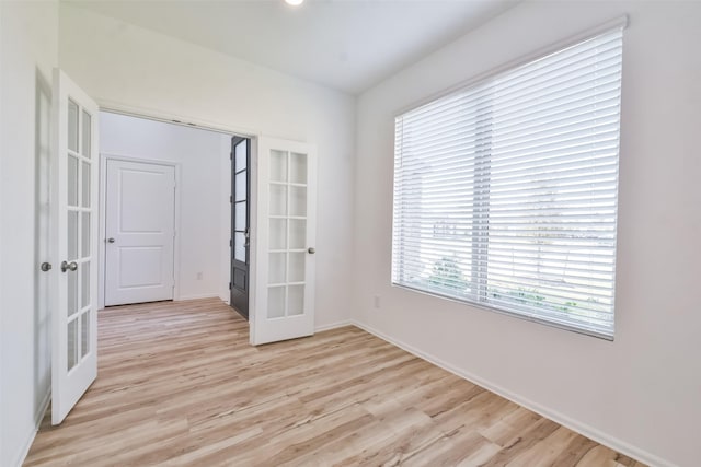 empty room with plenty of natural light, light hardwood / wood-style flooring, and french doors