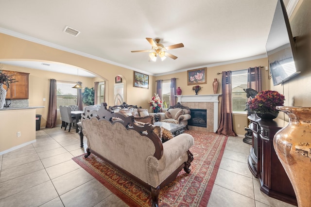 living room with ceiling fan, light tile patterned floors, crown molding, and a tile fireplace