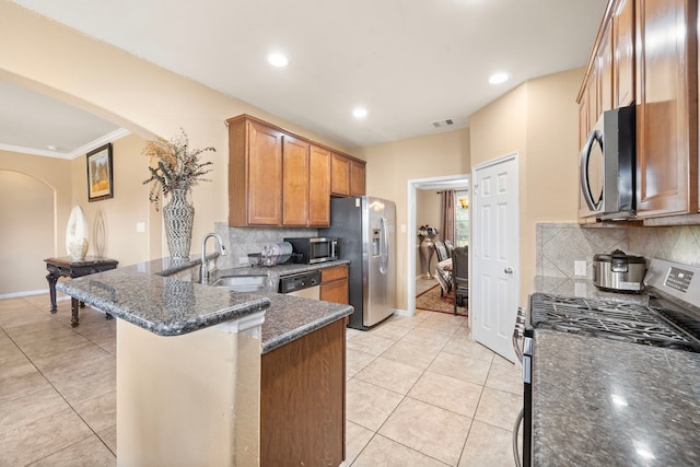 kitchen with sink, kitchen peninsula, dark stone countertops, decorative backsplash, and appliances with stainless steel finishes