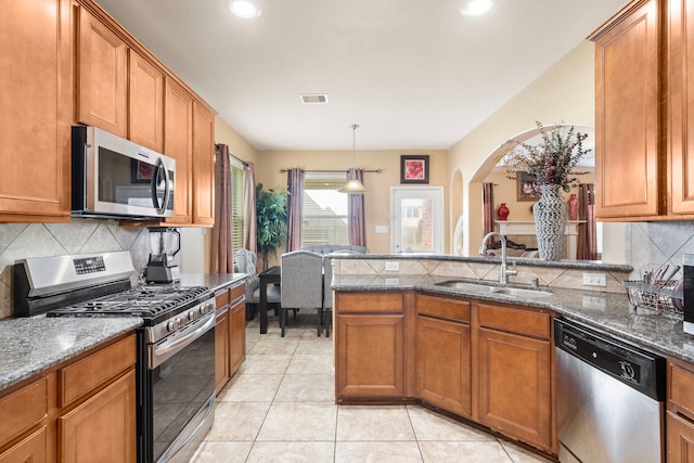 kitchen featuring appliances with stainless steel finishes, backsplash, sink, decorative light fixtures, and dark stone countertops