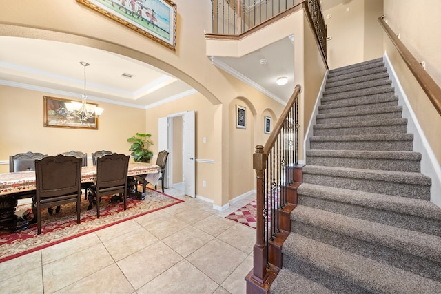 tiled foyer entrance featuring a raised ceiling, a towering ceiling, a notable chandelier, and ornamental molding