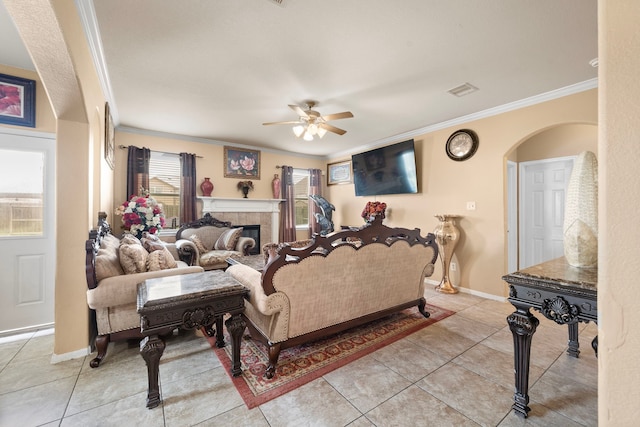 tiled living room featuring ceiling fan, crown molding, and a tile fireplace