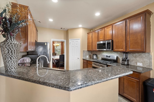 kitchen featuring dark stone counters, sink, decorative backsplash, kitchen peninsula, and stainless steel appliances