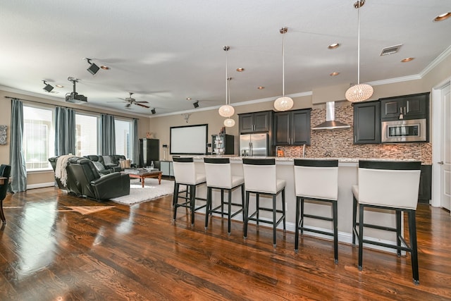 kitchen featuring a kitchen breakfast bar, stainless steel appliances, a large island with sink, and wall chimney range hood