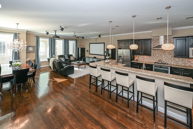 kitchen with pendant lighting, ceiling fan with notable chandelier, decorative backsplash, a kitchen bar, and stainless steel appliances