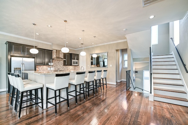 kitchen featuring a breakfast bar, dark brown cabinetry, wall chimney range hood, pendant lighting, and a large island