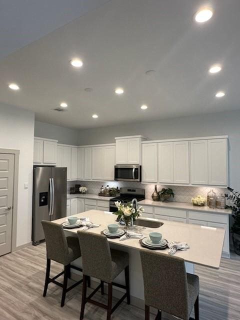 kitchen with sink, white cabinets, stainless steel appliances, and a center island with sink