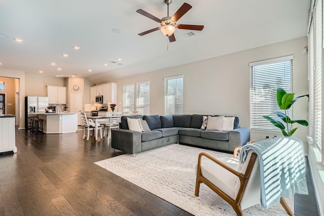 living room with dark wood-type flooring, ceiling fan, and a healthy amount of sunlight