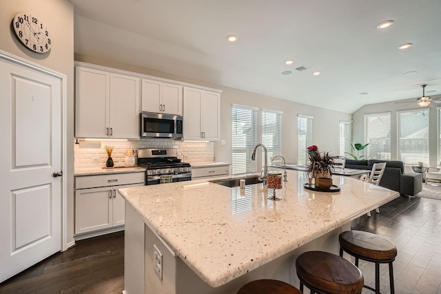 kitchen featuring stainless steel appliances, ceiling fan, sink, white cabinetry, and an island with sink