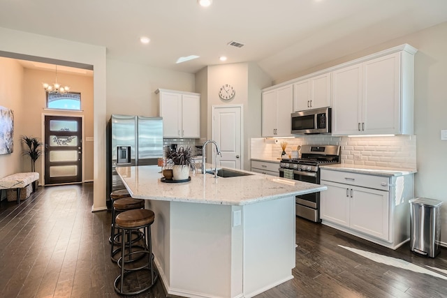 kitchen featuring stainless steel appliances, sink, a center island with sink, a notable chandelier, and white cabinetry