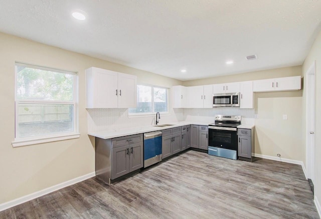 kitchen featuring white cabinetry, stainless steel appliances, sink, gray cabinets, and light hardwood / wood-style flooring