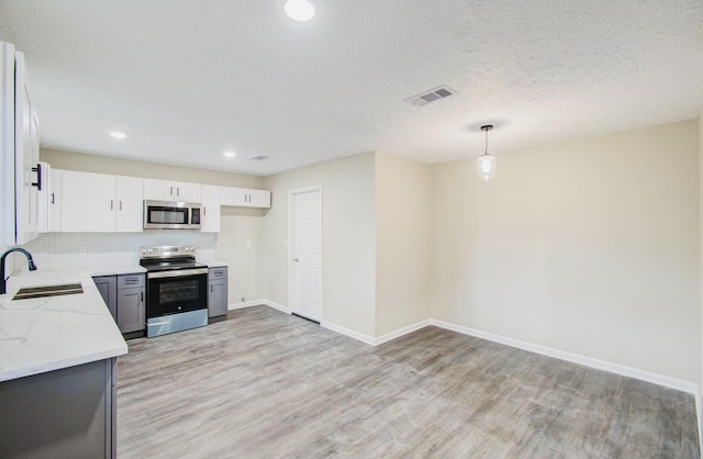 kitchen featuring pendant lighting, sink, light stone countertops, stainless steel appliances, and white cabinets