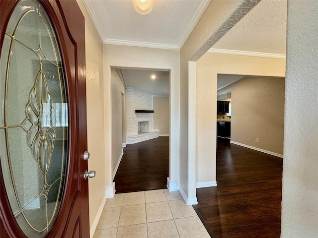 tiled foyer entrance featuring a brick fireplace, a textured ceiling, and ornamental molding