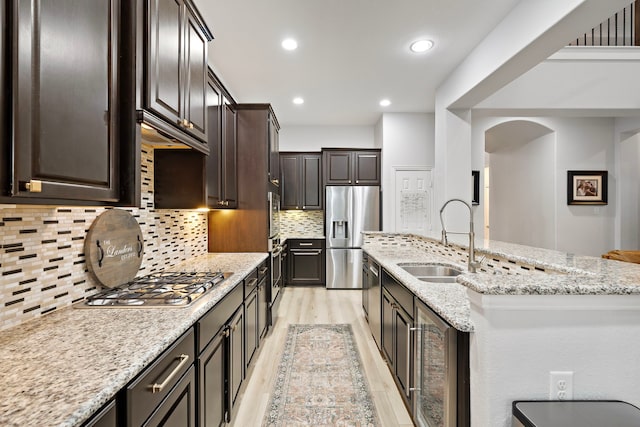 kitchen with sink, decorative backsplash, light stone countertops, dark brown cabinetry, and stainless steel appliances