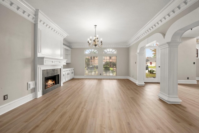 unfurnished living room featuring a chandelier, ornate columns, light hardwood / wood-style floors, crown molding, and a fireplace