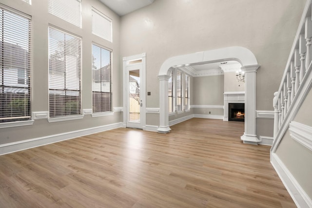 unfurnished living room featuring decorative columns, an inviting chandelier, and light hardwood / wood-style flooring