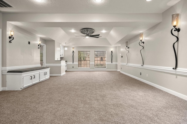 unfurnished living room featuring a textured ceiling, carpet floors, ceiling fan, and a raised ceiling