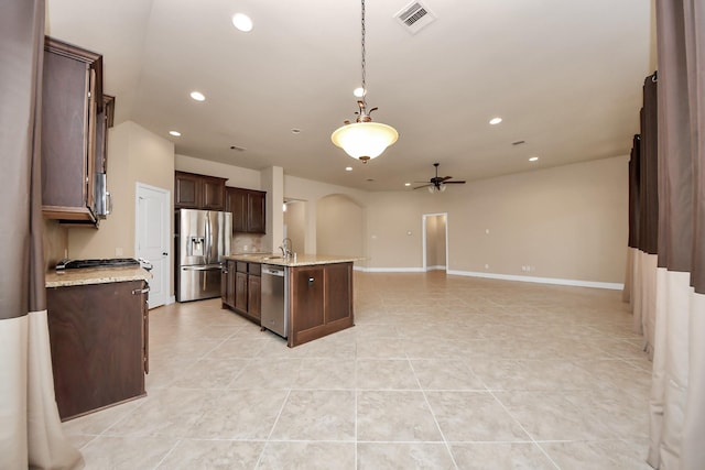 kitchen featuring dark brown cabinetry, stainless steel appliances, ceiling fan, pendant lighting, and an island with sink