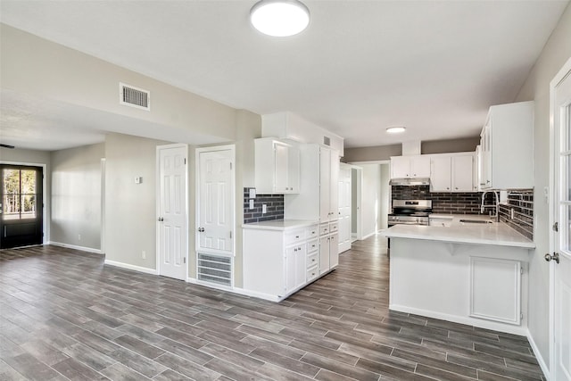 kitchen featuring kitchen peninsula, tasteful backsplash, sink, stainless steel range oven, and white cabinetry