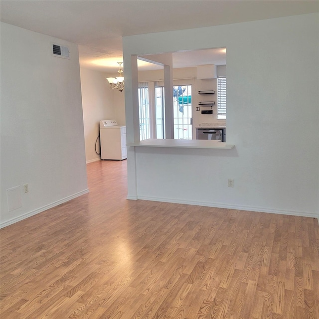 unfurnished living room with washer / dryer, light hardwood / wood-style floors, and a notable chandelier