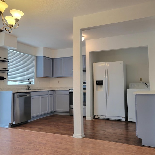 kitchen featuring sink, a notable chandelier, dark hardwood / wood-style flooring, washer / dryer, and stainless steel appliances