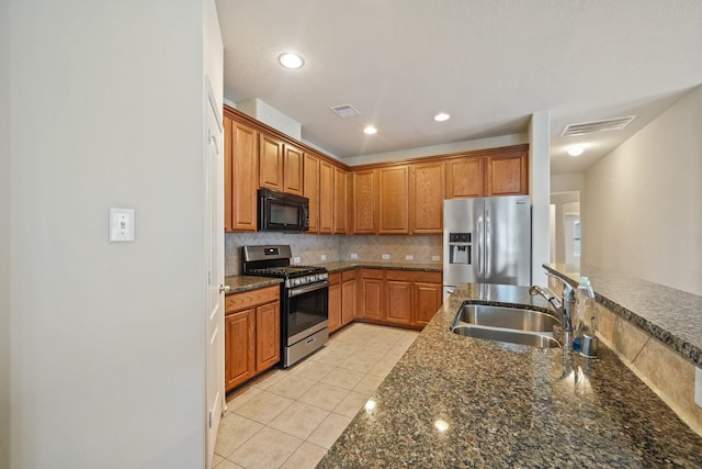 kitchen with tasteful backsplash, dark stone counters, stainless steel appliances, sink, and light tile patterned floors