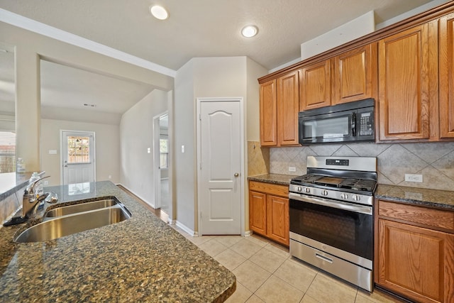 kitchen featuring backsplash, dark stone counters, sink, light tile patterned floors, and gas stove