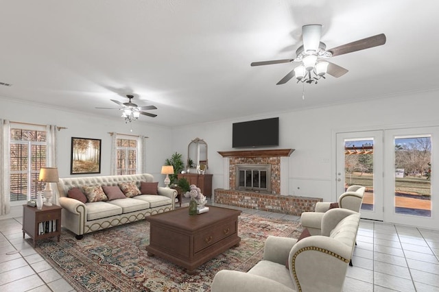 living room featuring a brick fireplace, ceiling fan, light tile patterned flooring, and ornamental molding