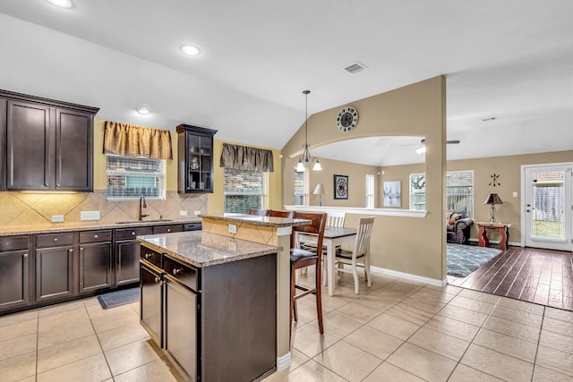 kitchen featuring a center island, a kitchen breakfast bar, sink, vaulted ceiling, and light stone countertops