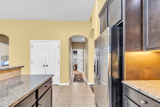 kitchen featuring dark brown cabinetry, light stone countertops, light tile patterned floors, and stainless steel refrigerator with ice dispenser