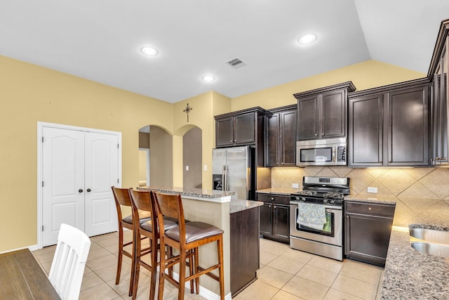 kitchen featuring light stone countertops, appliances with stainless steel finishes, a kitchen bar, a center island, and light tile patterned flooring