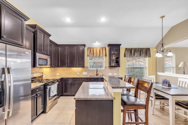 kitchen featuring light stone countertops, appliances with stainless steel finishes, decorative light fixtures, a kitchen island, and lofted ceiling