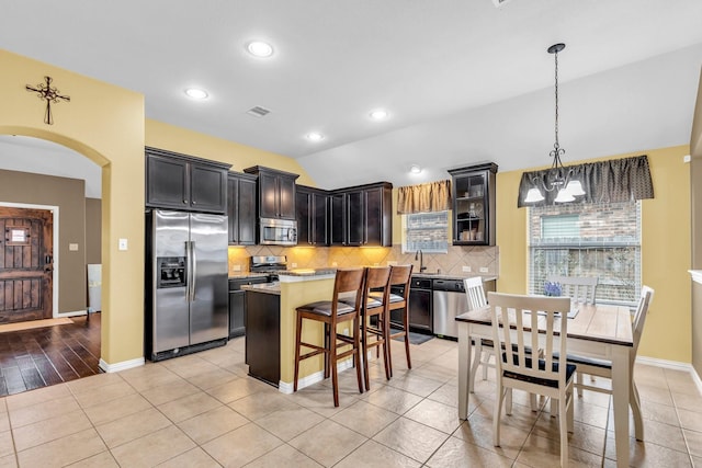 kitchen with hanging light fixtures, a notable chandelier, lofted ceiling, a kitchen island, and appliances with stainless steel finishes