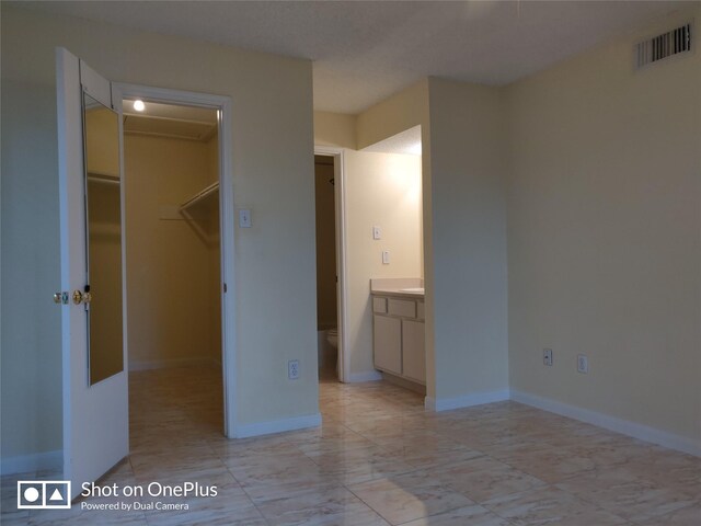 unfurnished bedroom featuring connected bathroom, a walk in closet, and a closet