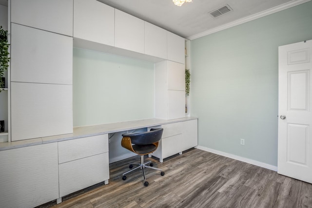 unfurnished office featuring built in desk, hardwood / wood-style flooring, and crown molding