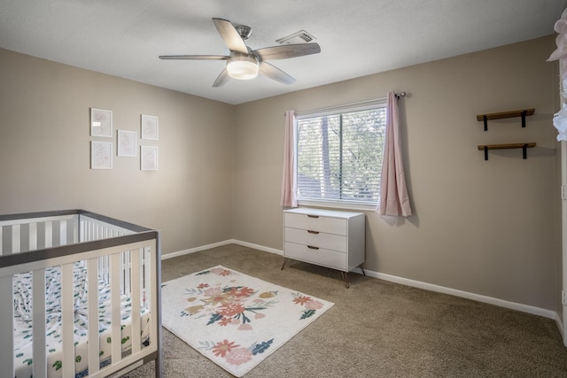 carpeted bedroom with a crib and ceiling fan