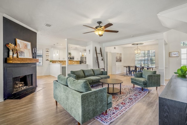 living room featuring crown molding, a fireplace, light hardwood / wood-style floors, and ceiling fan with notable chandelier