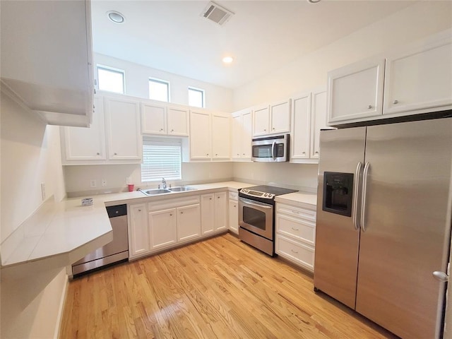 kitchen with white cabinets, light wood-type flooring, stainless steel appliances, and sink