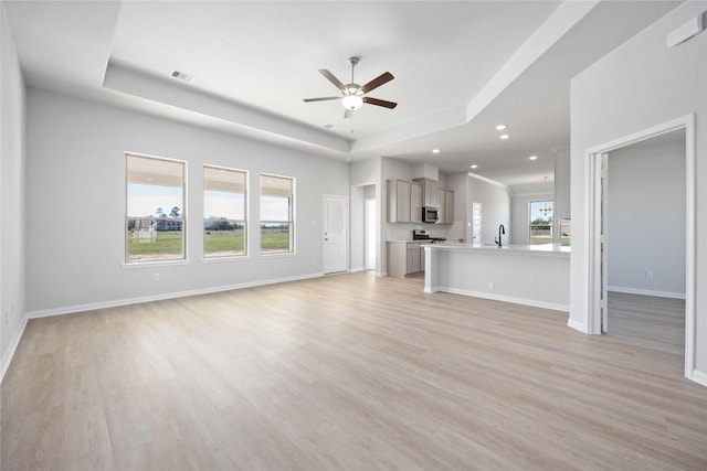 unfurnished living room featuring a tray ceiling, ceiling fan, and light hardwood / wood-style floors