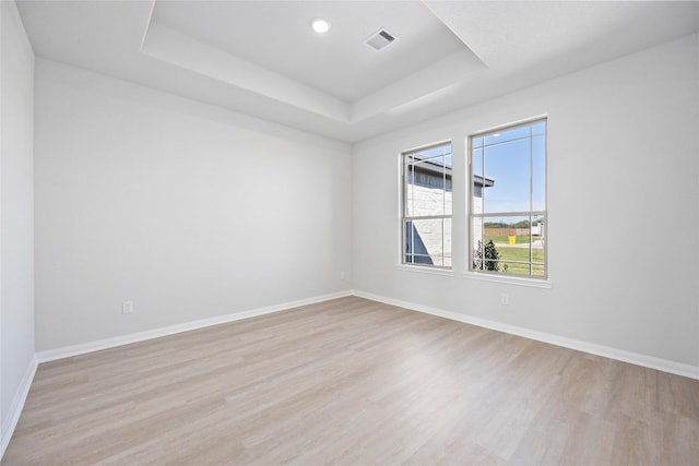 empty room with a tray ceiling and light hardwood / wood-style flooring