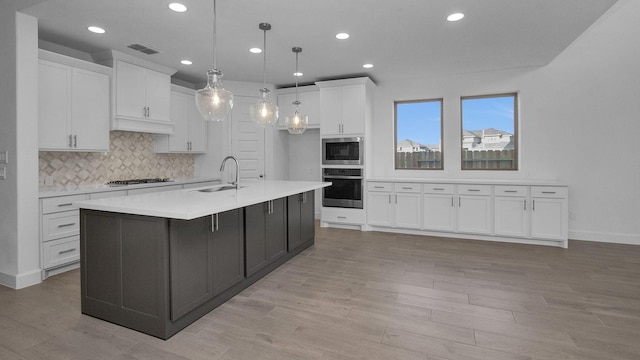 kitchen featuring white cabinetry, hanging light fixtures, sink, stainless steel appliances, and a large island with sink