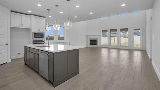 kitchen with built in microwave, dishwasher, a kitchen island with sink, white cabinets, and sink