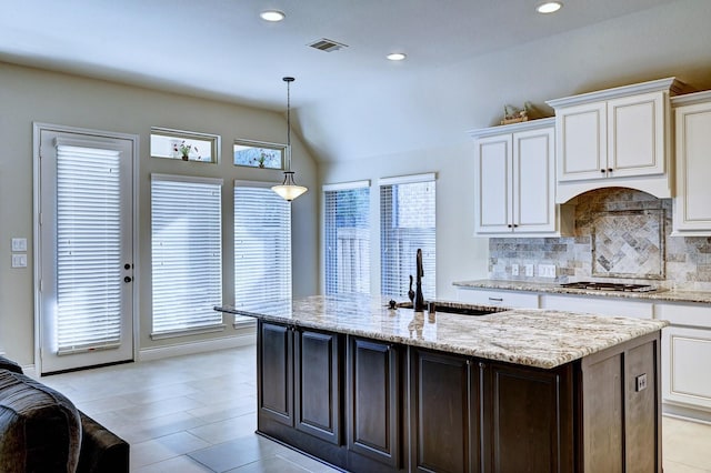 kitchen featuring lofted ceiling, hanging light fixtures, an island with sink, tasteful backsplash, and dark brown cabinetry