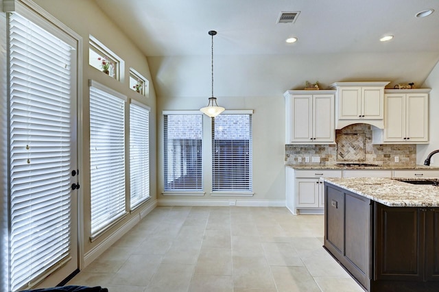 kitchen featuring decorative backsplash, light stone counters, white cabinets, lofted ceiling, and light tile patterned flooring