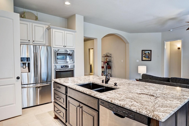 kitchen featuring light stone countertops, stainless steel appliances, a kitchen island with sink, sink, and white cabinetry