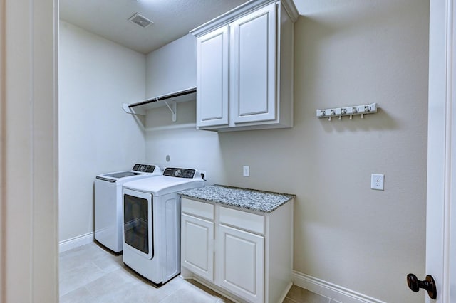 clothes washing area with washer and clothes dryer, cabinets, and light tile patterned floors