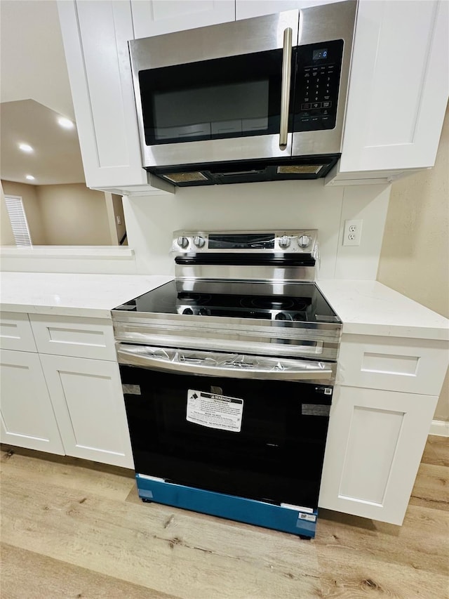 kitchen with white cabinets, appliances with stainless steel finishes, and light hardwood / wood-style flooring