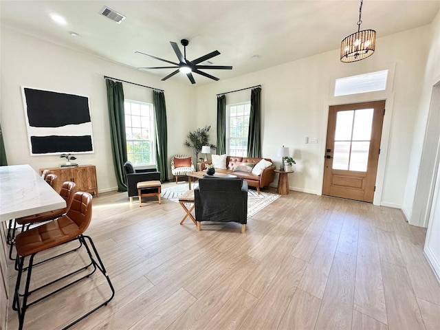 living room with ceiling fan with notable chandelier and light hardwood / wood-style flooring