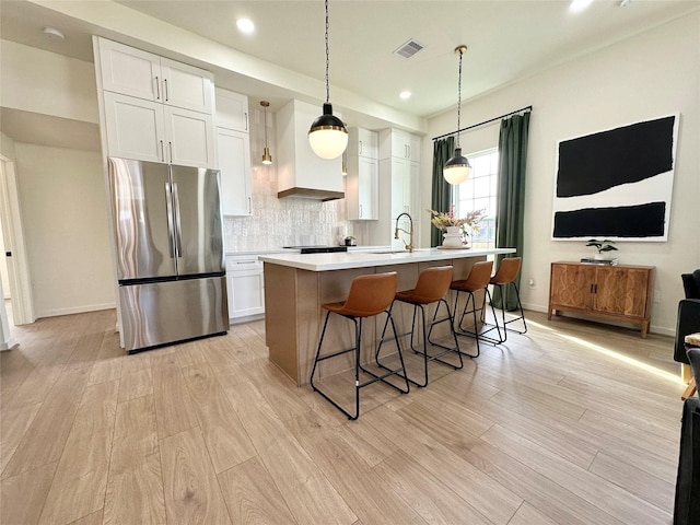 kitchen with visible vents, white cabinetry, light countertops, light wood-type flooring, and freestanding refrigerator